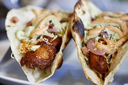 Close up of a fried walleye fish taco with lettuce, salsa, onion, tomato and sauce and shallow depth of field